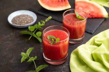 Watermelon juice with chia seeds and mint in glass on a black concrete background with green textile. Side view,  selective focus.