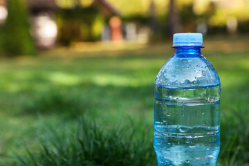 Plastic bottle of water on green grass outdoors, closeup. Space for text