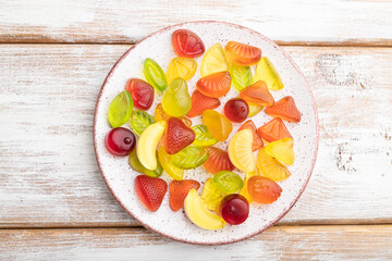 Various fruit candies on plate on white wooden background. close up, top view.