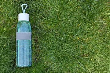 Glass bottle of fresh water on green grass outdoors, top view. Space for text