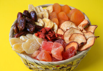 Wicker basket with different dried fruits on yellow background, closeup