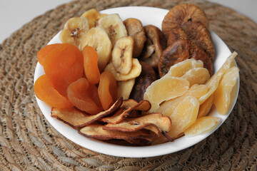 Bowl with different dried fruits on wicker mat, closeup