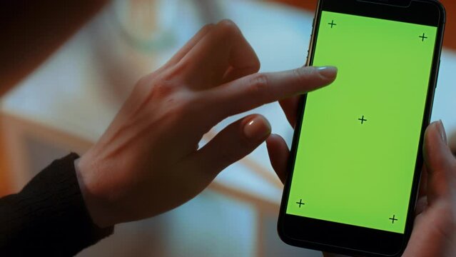 (Camera used: ARRI ALEXA, 50mm lens, slow motion) Slow pan of a Caucasian woman holding a green screen cell phone with tracking marks as she scrolls downwards with her finger twice.
