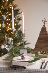Festive place setting with beautiful dishware, cutlery and gingerbread house card holder for Christmas dinner on wooden table