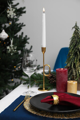 Festive place setting with beautiful dishware, candle and fabric napkin for Christmas dinner on white table