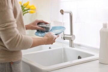 Woman washing plate above sink in modern kitchen, closeup