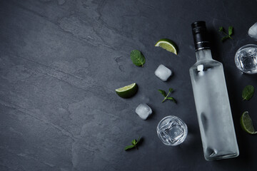 Bottle of vodka, shot glasses, lime, mint and ice on black table, flat lay. Space for text