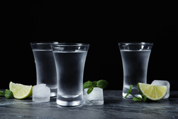 Shot glasses of vodka with lime slices, ice and mint on grey table