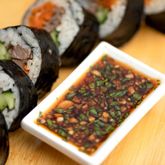 Sushi rolls with beef and vegetables on table. Gravy boat with sauce and fresh herbs. Roll supply. Japanese kitchen. Healthy diet. Close-up. Soft focus. High quality photo