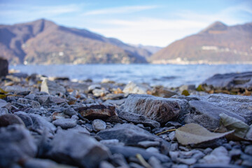 Low Angle View of Gravel beach with tree trunks on Maggiore Lake. Luino, Italy