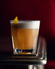 Alcoholic citrus drink in glass with foam, decorated with citrus. Drink on wooden table. Maroon background. Soft focus. Close-up. Side view. Copy space.