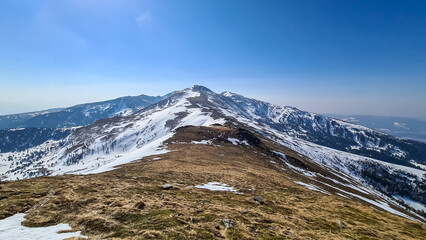 Fototapeta premium Ascent over snow covered alpine pasture to mountain peak Scharfes Eck near Zirbitzkogel, Seetal Alps, Styria (Steiermark), Austria, Europe. Idyllic hiking trail on ridges in sunny early spring
