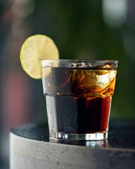 Fresh made Cuba Libre alcoholic cocktail with brown rum, cola and lime. Glass of alcoholic drink on table. Blurred dark background. Soft focus. Copy space.