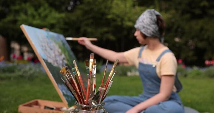 Art studio in the garden . Oil paintings. Canvas on easel. Set of different sized dirty brushes. Landscape art painting