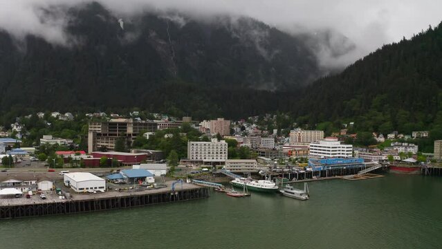 Aerial backwards shot of Juneau City with Marina and dense clouds hovering in green mountains of Alaska