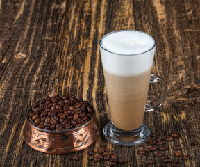 Latte macchiato in beautiful cup on wooden background with natural shadow. Cappuccino frothy coffee...