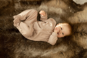 An Asian child lies on his back on a warm reindeer skin with thick and dense fur and holds his fist in his mouth