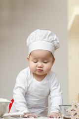 An Asian baby in a chef's cap and apron, smeared in flour, prepares Christmas ginger cookies