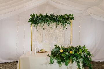 Festive table, arch decorated leaves eucalyptus greenery and garland with lights in tent. Hall with decor herbs and lemons. Luxury stand newlyweds in banquet area on wedding party. Setup for ceremony.