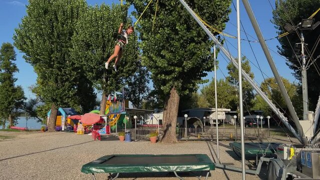 Happy little kid girls trying to back flip while bouncing on trampoline with harness