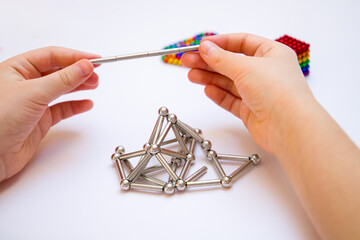 The child's hands hold a constructor consisting of magnetic sticks and balls