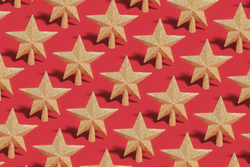 Pattern of golden glittering star shaped Christmas ornament on red backround.