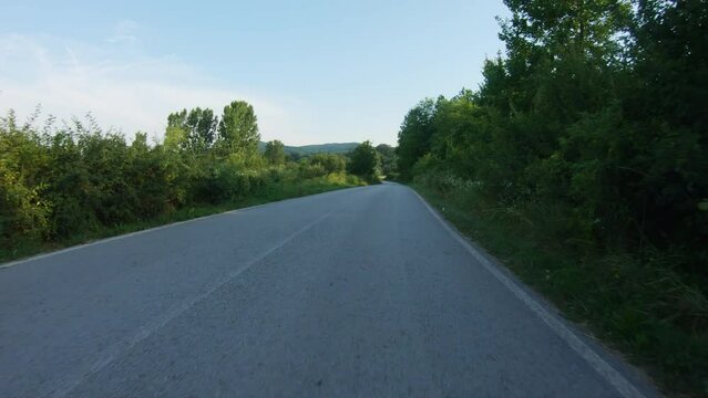 A slow ride of a car or motorcycle downhill on a winding country road in the shade of trees. Blue sky, summer time. POV shot