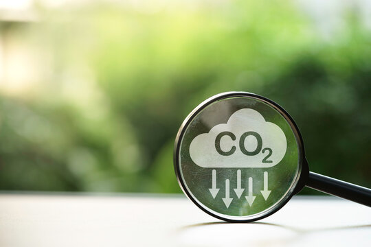 CO2 reducing icon inside magnifier glass on greenery background for decrease CO2 , carbon footprint and carbon credit to limit global warming from climate change, Bio Circular Green Economy concept.