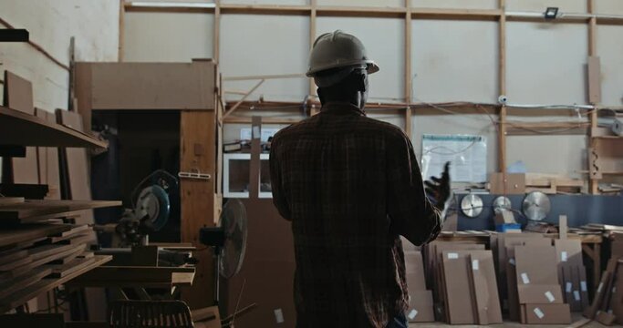 African carpenter on a business call in the factory, discussing plans on mobile phone