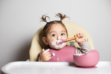 Small cute little toddler brunette caucasian girl with two tails tasting and enjoying by herself...