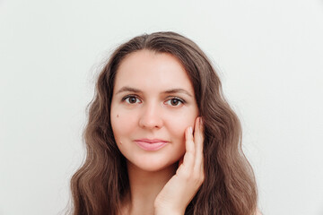 Fototapeta premium Portrait of beautiful brown hair young woman, touching her face. Scin care, natural beauty, perfect skin,cosmetics and wellness concept. Studio shot, white background.