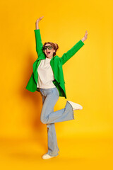 Portrait of young happy girl in bright green jacket posing in excitement over yellow studio background. Happiness