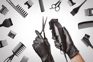 Hairdressers hands in black rubber gloves holds hair clipper and scissors surrounded by professional hairdressing accessories, close up