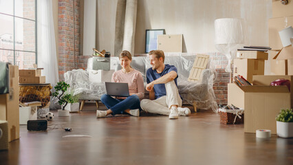 Happy Young Homeowners: Lovely Couple Sitting on Floor of the Newly Purchased Apartment Use Laptop...