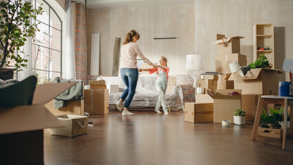 Fototapeta premium Happy Mother and Daughter Moving Into their New Cozy Home. Cheerful Young Family, Happy Girls Have Fun, Dance, Hug in the Middle of Apartment. Living Room Has Unpacked Cardboard Boxes, Furniture