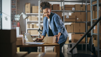 Warehouse Female Worker Using Laptop Computer, Preparing a Small Parcel for Shipping. African American Small Business Owner Working in Storeroom, Preparing Order for Client.