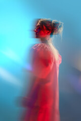 Portrait of young beautiful girl in white dress posing over blue background in neon lights....