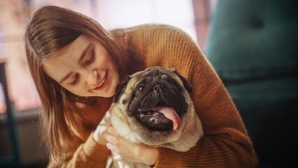 Beautiful Young Woman Cuddles Her Adorable Little Pug at Home. Girl Plays with Her Dog, Gorgeous Pedegree Best Friend. She Pets and Scratches Super Happy Doggy, Have Fun in the Living Room.