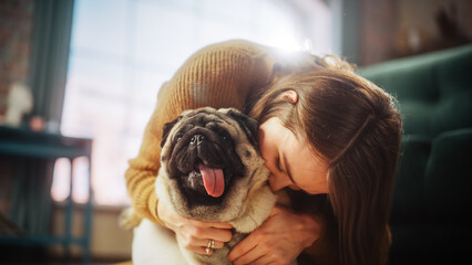 Portrait of Beautiful Young Woman Cuddles Her Adorable Little Pug at Home. Girl Plays with Her Dog,...