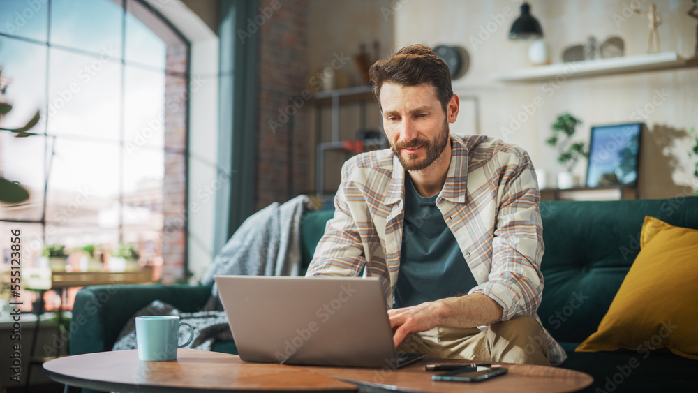Poster portrait of smiling middle aged man working from home on a laptop computer in sunny cozy apartment. 