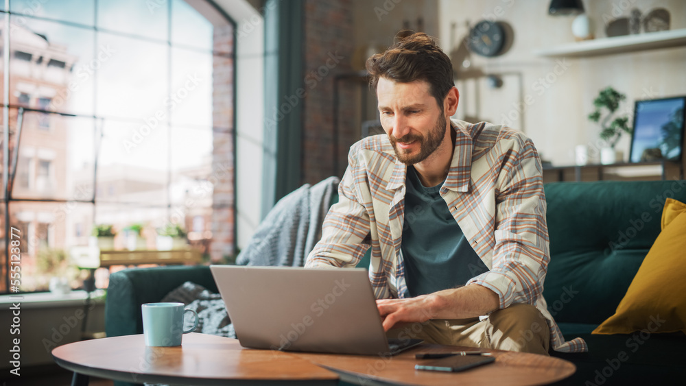 Poster portrait of smiling middle aged man working from home on a laptop computer in sunny cozy apartment. 