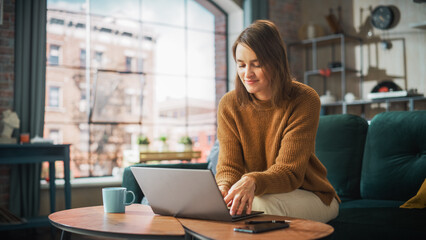 Portrait of Smiling Young Woman Working from Home on Laptop Computer in Sunny Cozy Apartment....