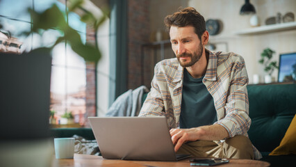 Fototapeta premium Portrait of Smiling Middle Aged Man Working from Home on a Laptop Computer in Sunny Cozy Apartment. Successful Male Entrepreneur Does Remote for e-Business Project, Online Shopping