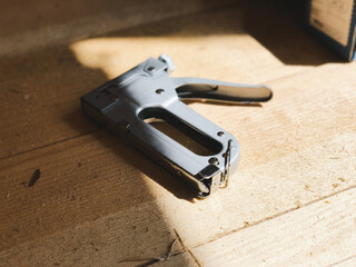 Construction gray stapler lies on a wooden floor from planks under the rays of the sun