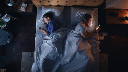 Top View Apartment Bedroom: Young Couple Lying in Bed, Both Using Smartphones. Family of Two Using...