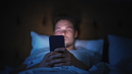 Caucasian Man Uses Smartphone in Bed at Home at Night. Handsome Guy Browsing Social Media, Reading...
