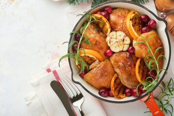 Baked chicken thighs with orange, cranberry and spicy herbs rosemary servered in frying pan on light background. Festive Christmas Dinner Concept menu. Top view. copy space