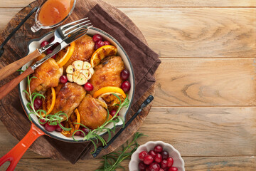 Baked chicken thighs with orange, cranberry and spicy herbs rosemary servered in frying pan on light wooden rustic background. Festive Christmas Dinner Concept menu. Top view. copy space