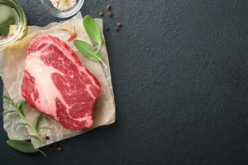 Raw beef steak. Raw fresh Chuck roll steak with rosemary, salt and pepper on cutting board on dark concrete background. Raw beef steak and spices for cooking.