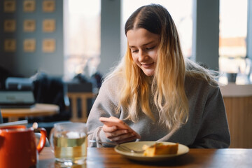 A young girl in a cafe uses the phone. People use technology. Cafe city lifestyle. Colorful portrait of happy pretty girl.